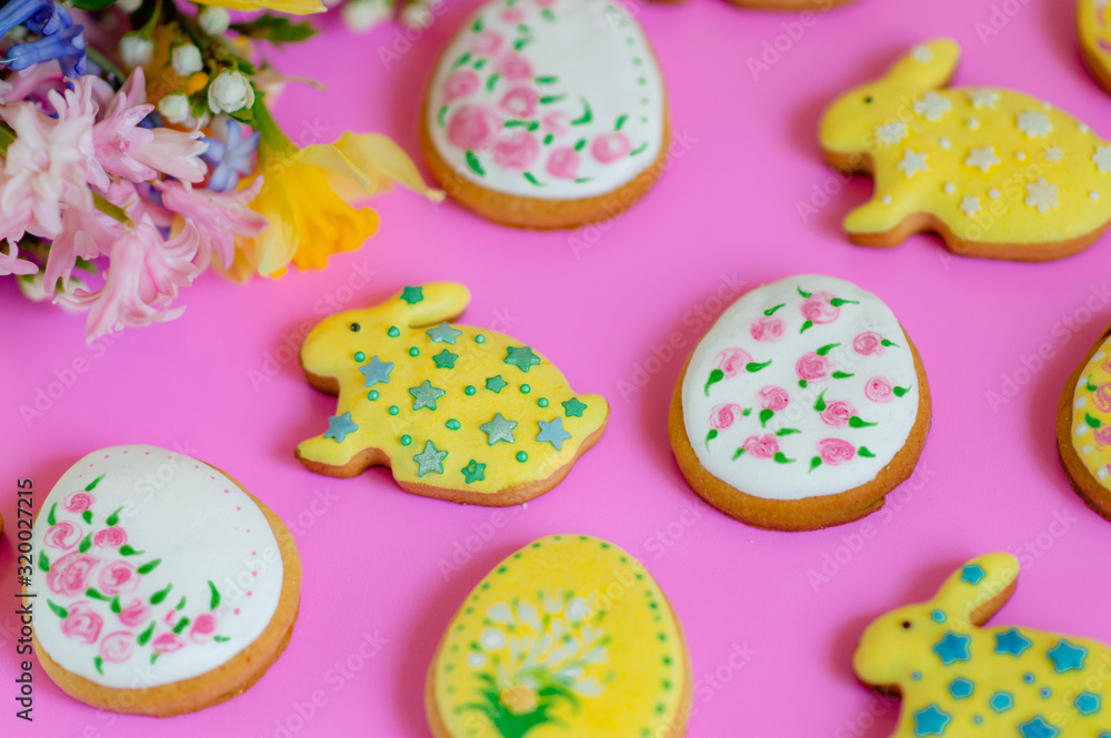 Flat lay of spring flowers and Easter ginger cookies in the shape of eggs and bunnies on a pink background.Happy Easter.Multi-colored pastel easter cookies on a pink background.Easter concept Flat lay of spring flowers and Easter ginger cookies in the shape of eggs and bunnies on a pink background.Happy Easter.Multi-colored pastel easter cookies on a pink background.Easter concept