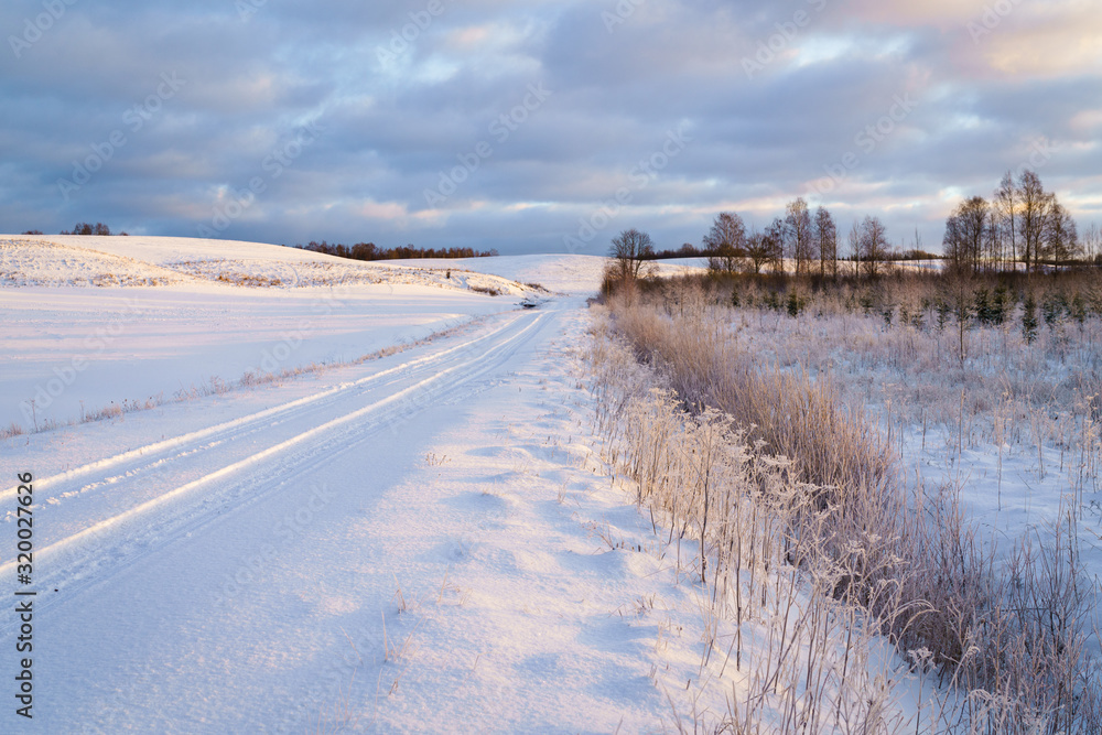 Winter morning, country road and fields covered with snow, in the distance you can see a hilly landscape.