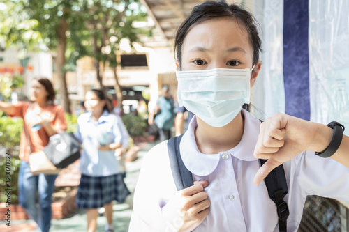Asian child girl student thumbs down with Thai school uniform wearing surgical mask to prevent Corona virus infection,dust,air pollution,Pm2.5,viruses,bacteria protection,Wuhan coronavirus 2019-nCoV