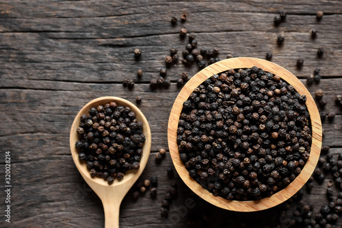 Black pepper seeds in a cup placed on old wooden table.