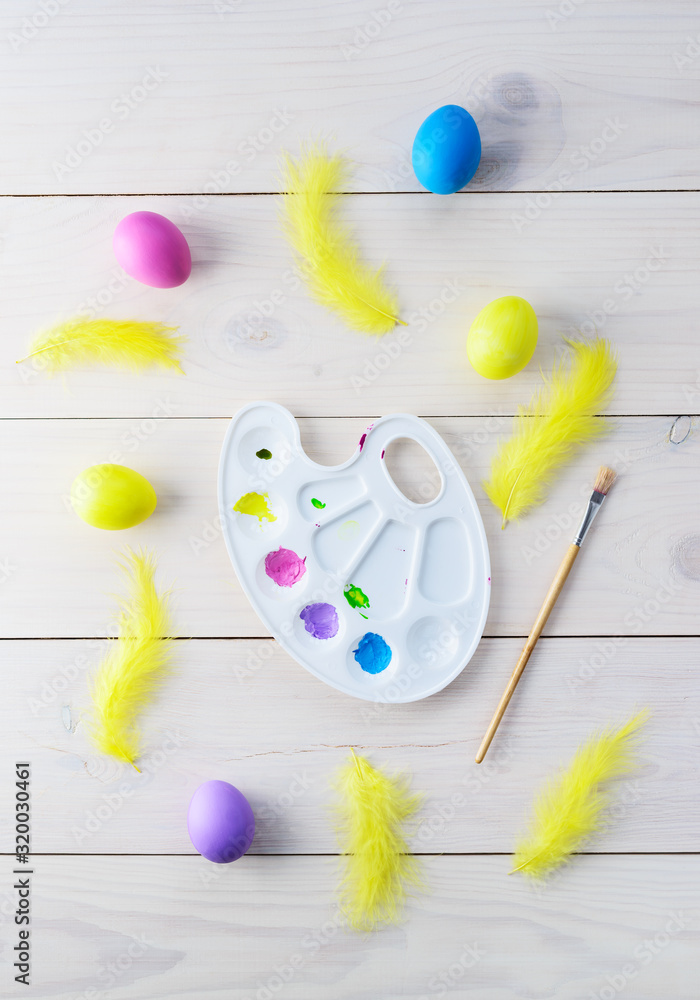 Easter eggs with feathers, palette and brush on a wooden table. Vertical orientation, top view. Easter eggs with feathers, palette and brush on a wooden table. Vertical orientation, top view.