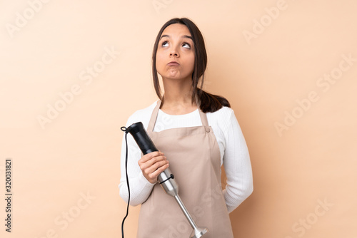 Young brunette girl using hand blender over isolated background and looking up