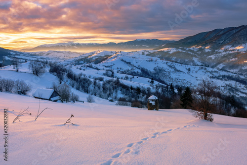 mountainous countryside in winter at sunrise. snow covered hills and fields of carpathian rural area rolling off in to the distant krasna ridge. glowing fog in the valley. colorful clouds on the sky