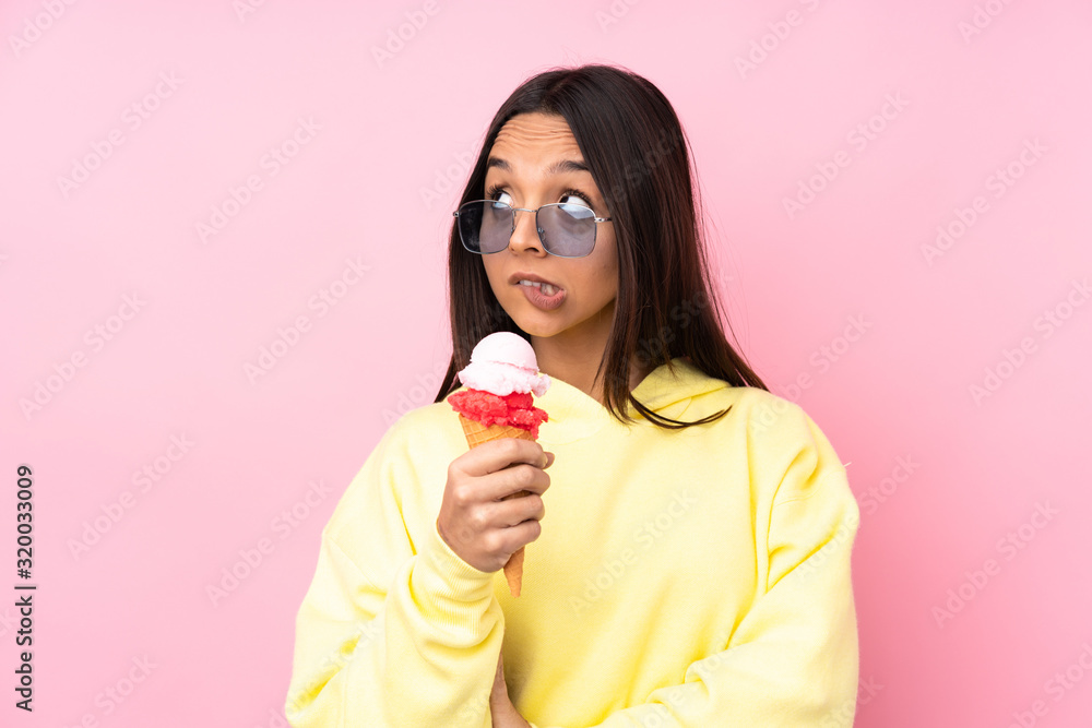 Young brunette girl holding a cornet ice cream over isolated pink background with confuse face expression Young brunette girl holding a cornet ice cream over isolated pink background with confuse face expression