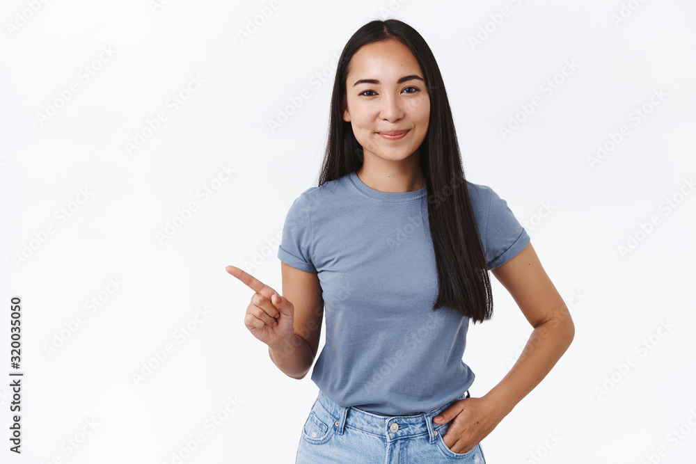 Carefree, outgoing good-looking lesbian asian girl in t-shirt, hold hand in  jeans pocket, pointing left and smiling, asking woman out for cup coffee,  standing white background, recommend product Stock Photo | Adobe