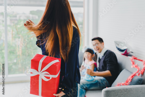 Mom holding a red gift box behind to the surprise Father and daughter. Concept Asian family happiness time.
