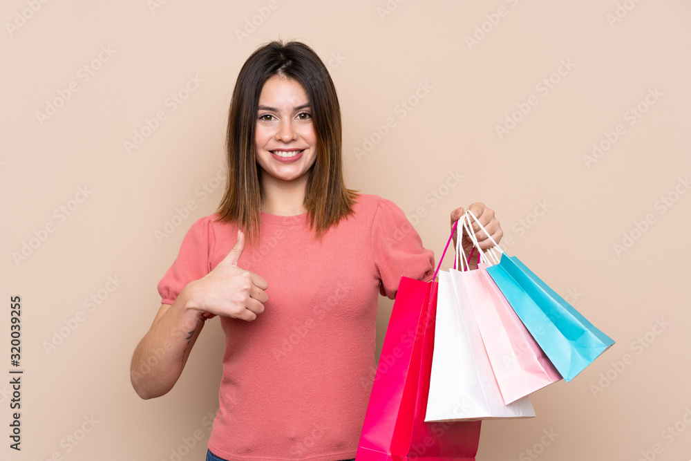 Young woman with shopping bag over isolated background with thumbs up because something good has happened Young woman with shopping bag over isolated background with thumbs up because something good has happened