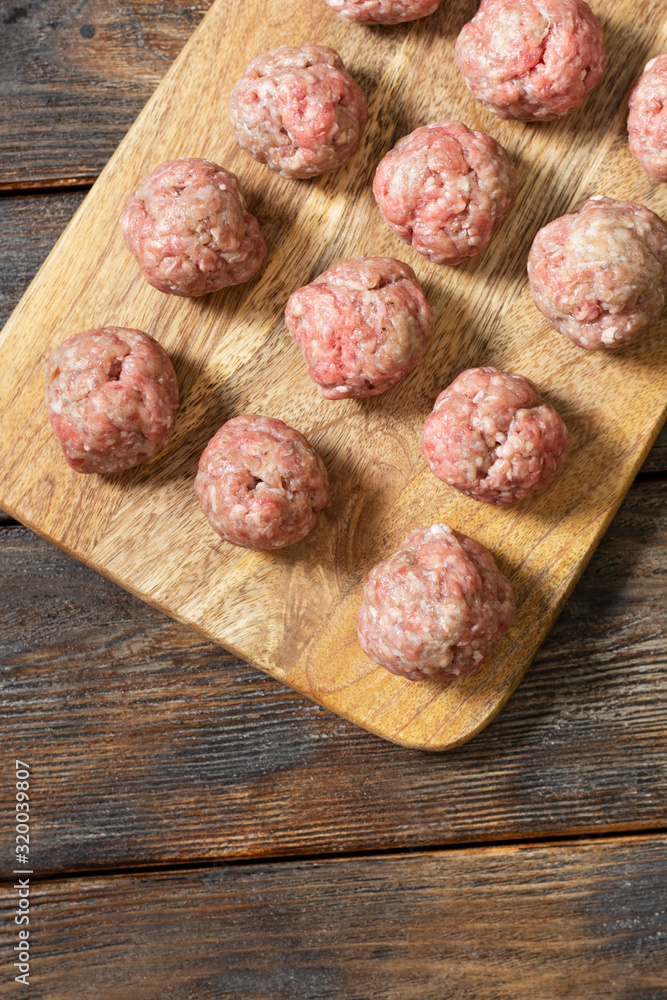 Raw meat meatballs on a wooden Board on a brown wooden table. Top view with a copy of the space