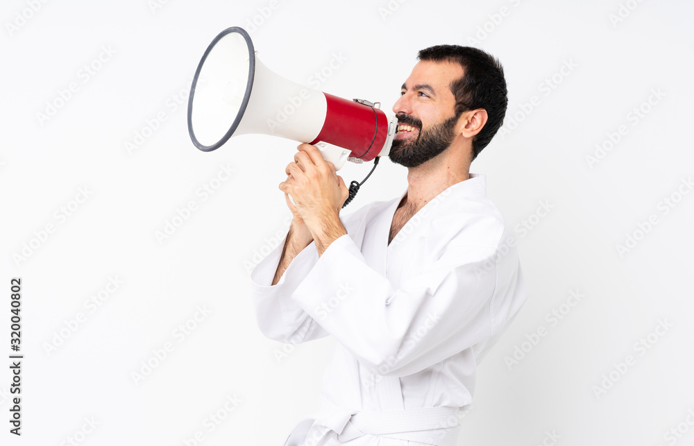 Young man doing karate over isolated white background shouting through a megaphone Young man doing karate over isolated white background shouting through a megaphone