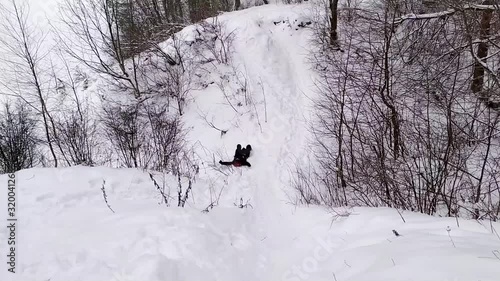 Winter fun of woman sliding down the snow hill in the forest on coat