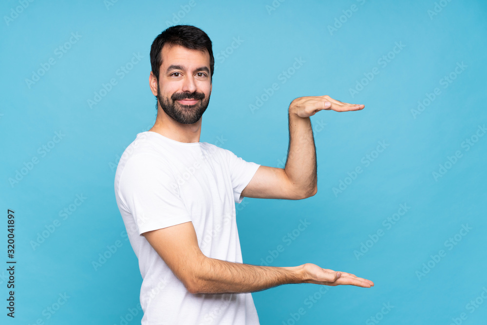 Young man with beard over isolated blue background holding copyspace to insert an ad Young man with beard over isolated blue background holding copyspace to insert an ad