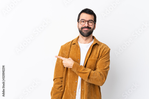 Caucasian handsome man with beard wearing a corduroy jacket over isolated white background pointing to the side to present a product