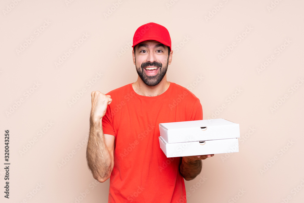 Young man holding a pizza over isolated background celebrating a victory in winner position Young man holding a pizza over isolated background celebrating a victory in winner position