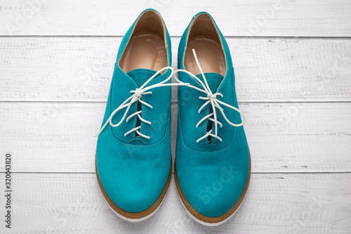 Pair of suede shoes aqua color. Green boots with white laces on a light wooden background, top view.