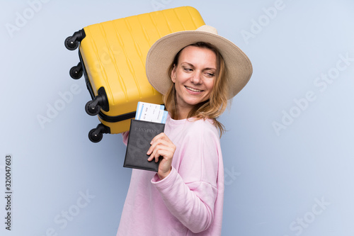 Blonde woman over isolated background in vacation with suitcase and passport