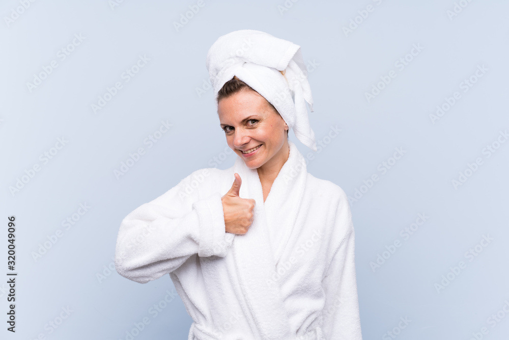 Woman in bathrobe over isolated blue background giving a thumbs up gesture Woman in bathrobe over isolated blue background giving a thumbs up gesture