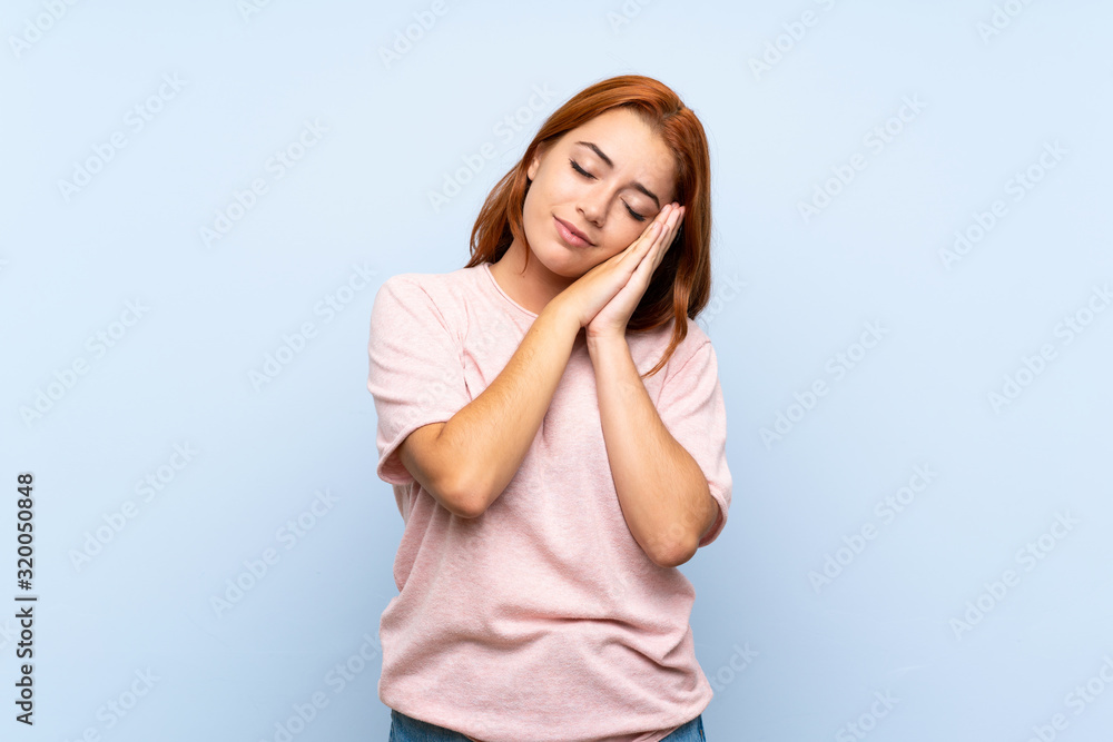 Teenager redhead girl over isolated blue background making sleep gesture in dorable expression Teenager redhead girl over isolated blue background making sleep gesture in dorable expression