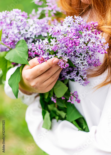Spring background. Flowers of lilac in the hands of a young girl in a white blouse. Close up, copy space