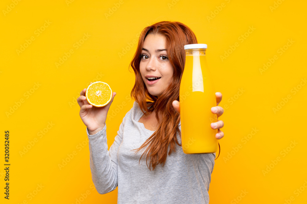 Teenager redhead girl holding an orange over isolated yellow background Teenager redhead girl holding an orange over isolated yellow background