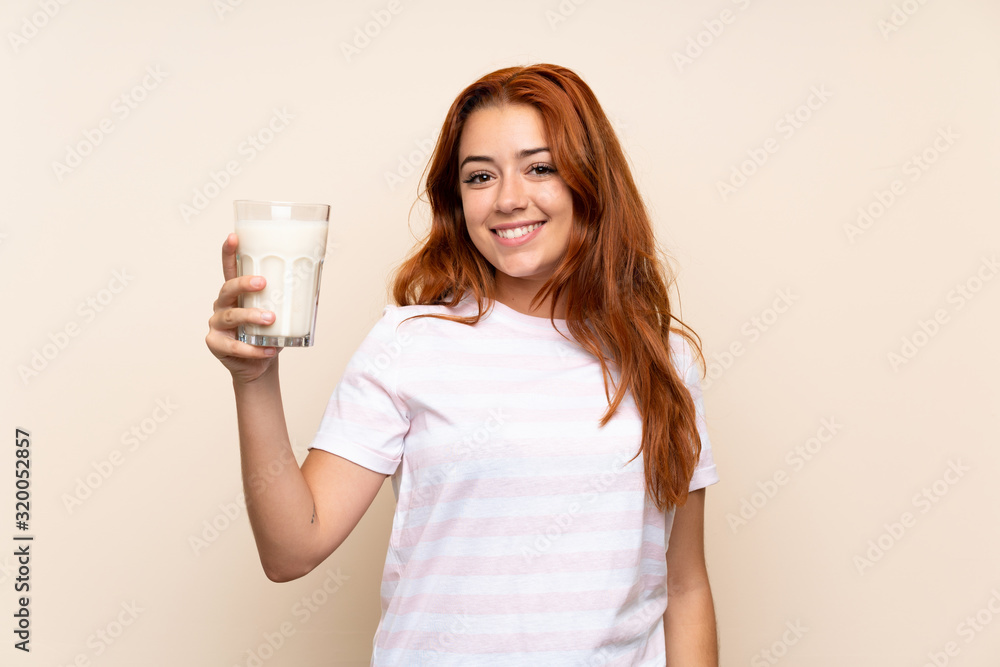 Teenager redhead girl holding a glass of milk over isolated background smiling a lot Teenager redhead girl holding a glass of milk over isolated background smiling a lot