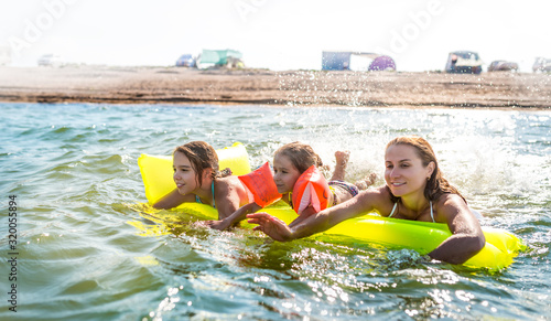 Charming young mother is swimming with her two happy little daughters in the lake on an air mattress on a warm summer day. Summer vacation concept © YouraPechkin