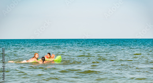 Rear view of a positive young family mom and two little daughters swim on a yellow air mattress in the sea on a sunny summer day during vacation. Relaxation concept. Copyspace