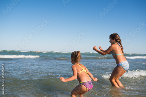 Two funny little girls jump in the noisy sea waves and enjoy the long-awaited vacation on a sunny warm summer day. Concept of sea vacation and travel with children