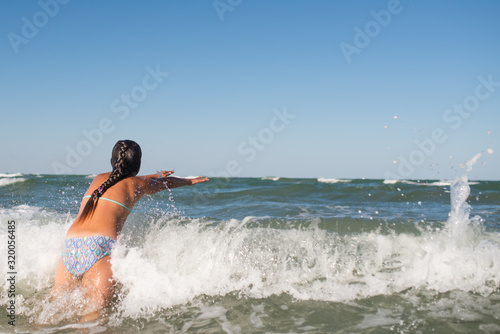Little funny active happy girl splashing in the noisy sea waves on a sunny warm summer day. Sea vacation concept with kids. Advertising space