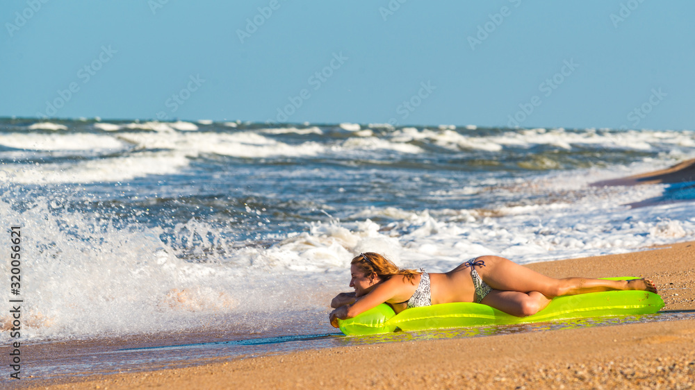 Beautiful young woman in a swimsuit sits on an air mattress on a sandy beach on a sunny hot summer day. Vacation and swimming concept. Copyspace Beautiful young woman in a swimsuit sits on an air mattress on a sandy beach on a sunny hot summer day. Vacation and swimming concept. Copyspace