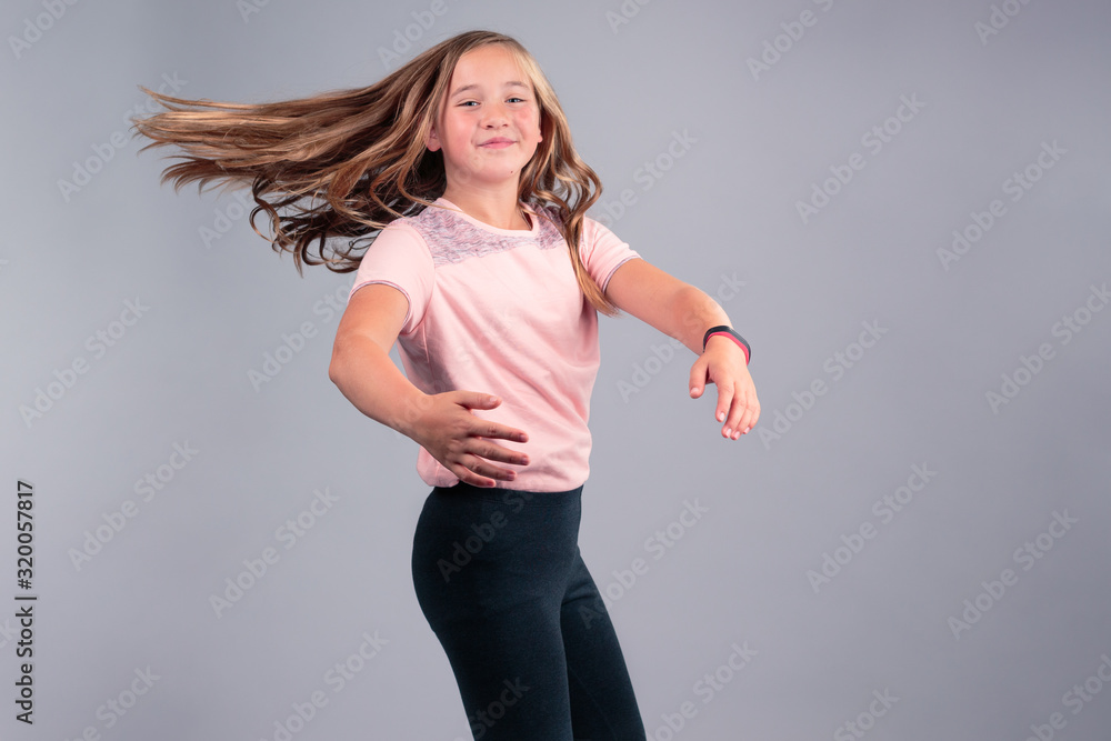 Cheerful 11 year old girl wearing pink t-shirt and black pants with waving  long blond hair dancing. isolated on grey background Stock Photo
