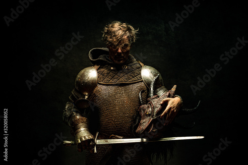 Foto Portrait of a knight in armor, his sword in his hand, holding a dragon head in t
