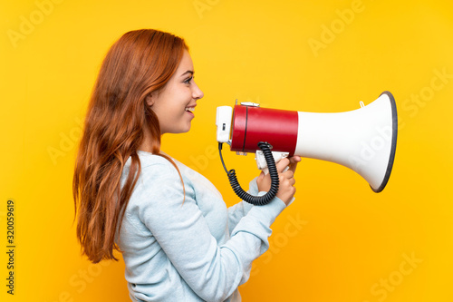 Teenager redhead girl over isolated yellow background shouting through a megaphone
