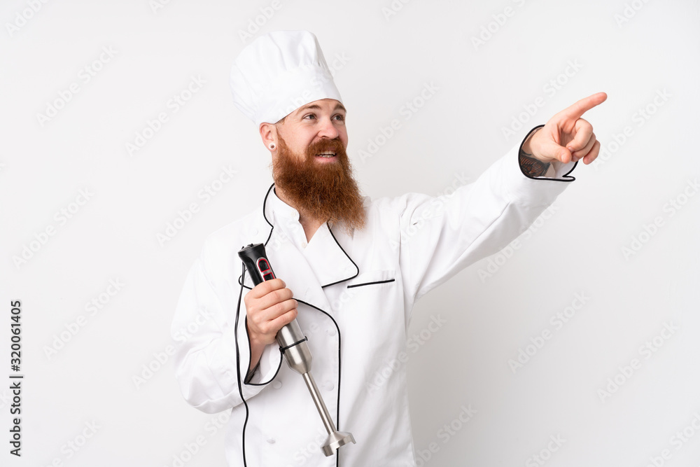 Redhead man using hand blender over isolated white background touching on transparent screen