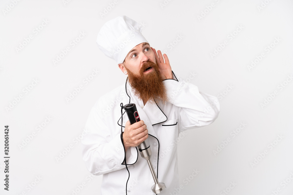 Redhead man using hand blender over isolated white background listening something Redhead man using hand blender over isolated white background listening something