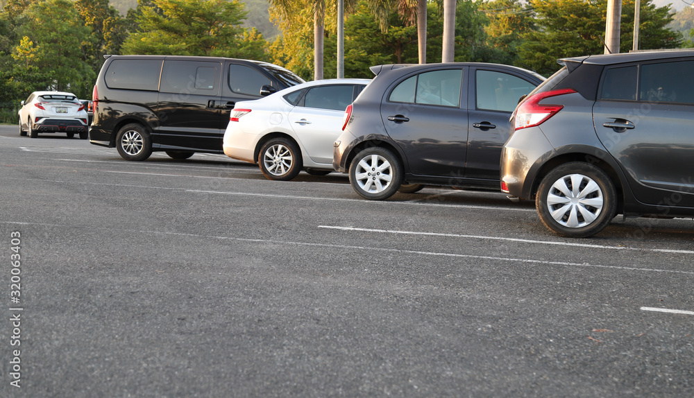 Fototapeta premium Closeup of rear, back side of dirty black car with sunlight and other cars parking in outdoor parking area in twilight evening.