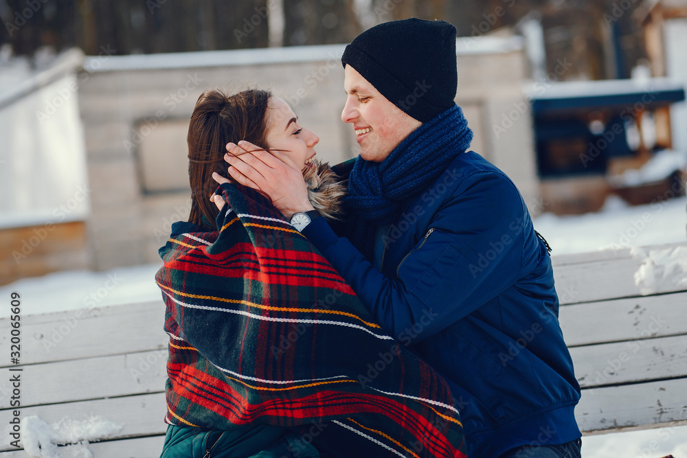 Young and loving couple sitting in a winter park with plaid