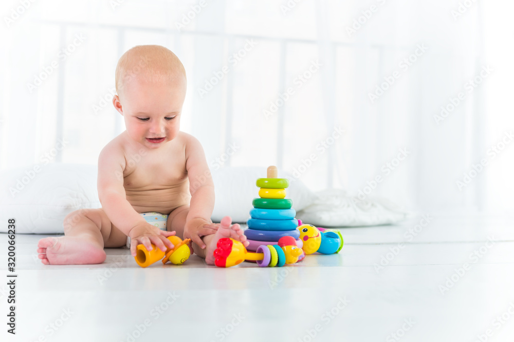 Charming cheerful kid in a diaper laughs and plays while sitting in his cozy room. The concept of a healthy happy baby and child care Charming cheerful kid in a diaper laughs and plays while sitting in his cozy room. The concept of a healthy happy baby and child care
