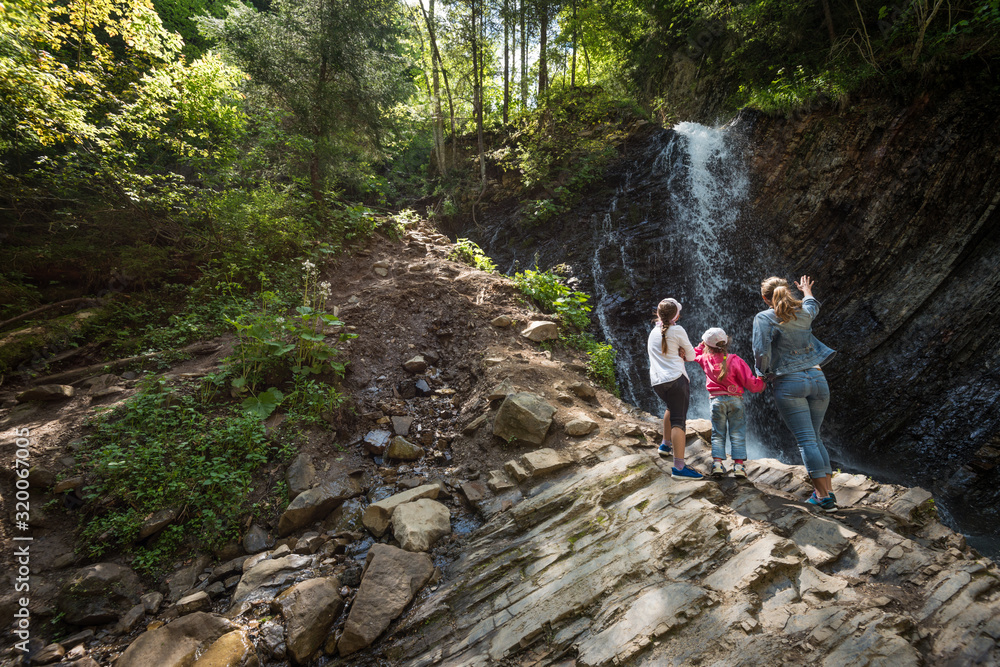 Young mother and children walk through the woods with a bewitching view of the natural expanses of the hills rock formations and a waterfall. Family vacation and trekking concept