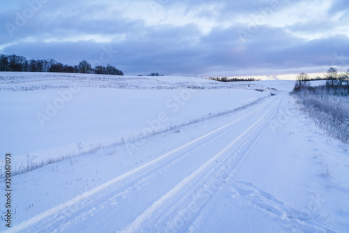 Winter morning, country road and fields covered with snow, in the distance you can see a hilly landscape. © Dainis