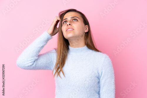 Teenager girl with blue sweater over isolated pink background having doubts and with confuse face expression