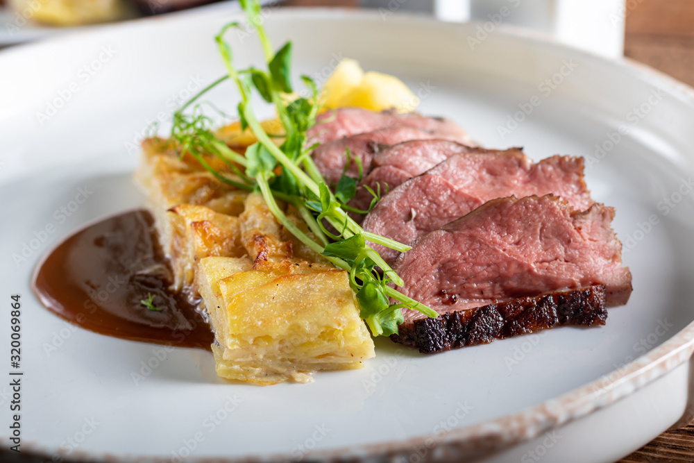 Duck breast with a side dish of potato casseroles, seasoned with pea microgreen with tomato and chili sauce. On a white plate. On a wooden background, Duck breast with a side dish of potato casseroles, seasoned with pea microgreen with tomato and chili sauce. On a white plate. On a wooden background,