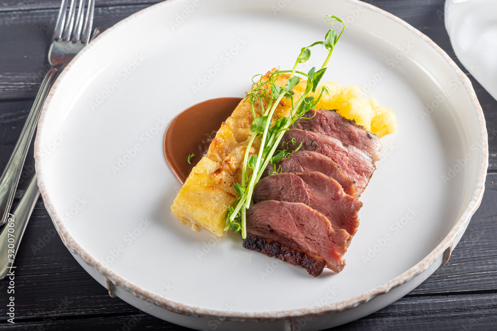 Duck breast with a side dish of potato casseroles, seasoned with pea microgreen with tomato and chili sauce. On a white plate. On a wooden background, Duck breast with a side dish of potato casseroles, seasoned with pea microgreen with tomato and chili sauce. On a white plate. On a wooden background,