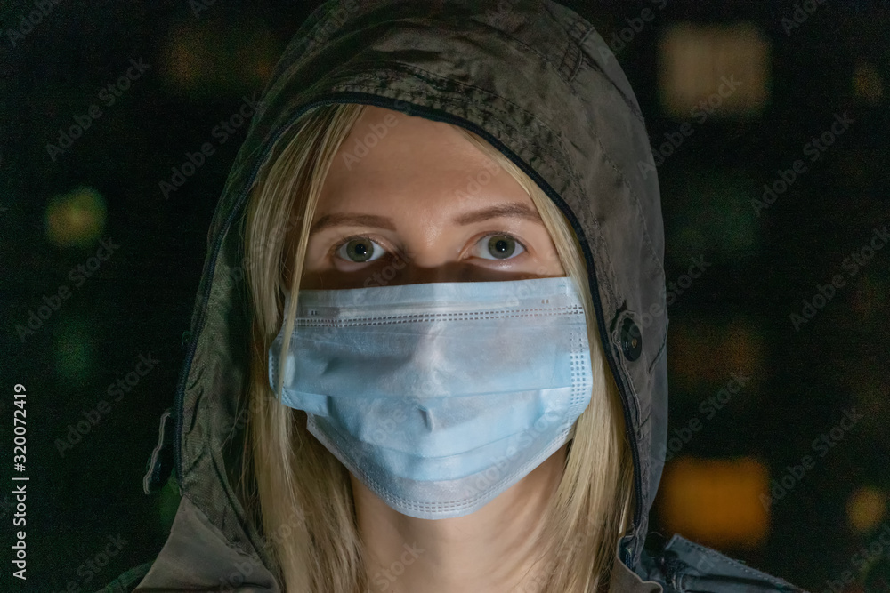 blonde girl in a hood with a medical mask on her face with the inscription coronavirus in the dark. Concept of health care, medicine blonde girl in a hood with a medical mask on her face with the inscription coronavirus in the dark. Concept of health care, medicine