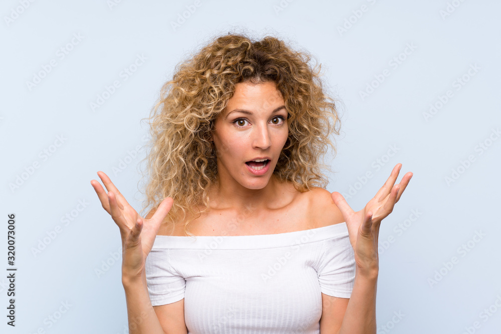 Young blonde woman with curly hair over isolated blue background unhappy and frustrated with something