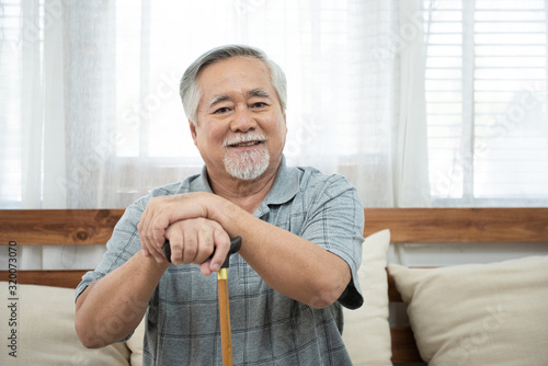 portrait of senior elderly asian man sit on coach hand hold walking stick look at camera with smile.