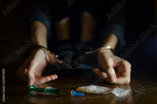 syringe and drugs with a defocused man sitting on the floor and his hands locked in handcuffs.Addict.