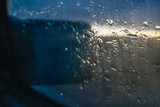 Water drops fall on the passenger window and mirror of the car on the background of the sunset
