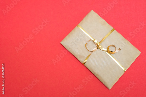 Craft gift wrap with gold ribbon on red background with copy space, top view