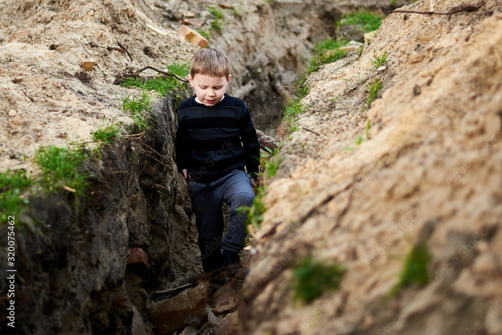 A trench dug in the ground in which a little boy plays.