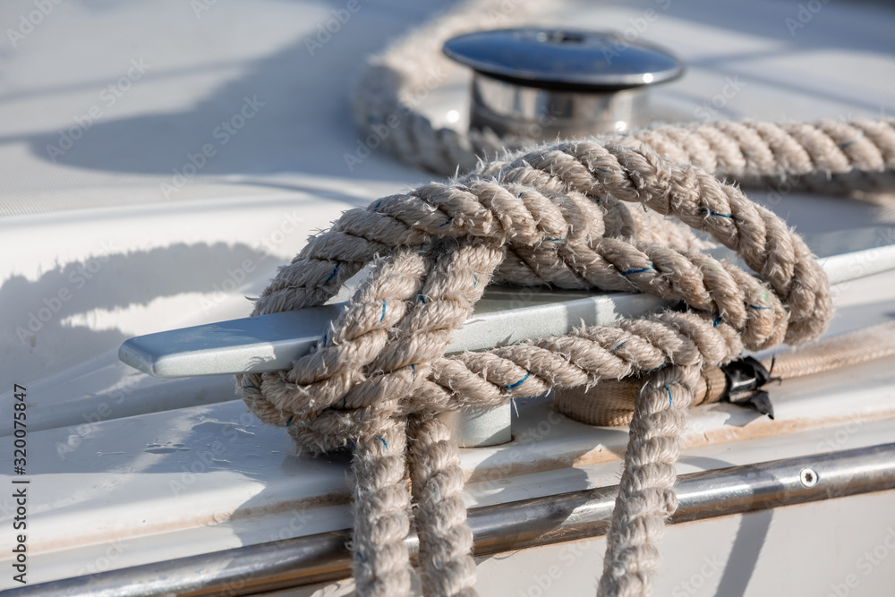 White and black sailing ropes spool closeup in figure eight tied on cleat, winch on background